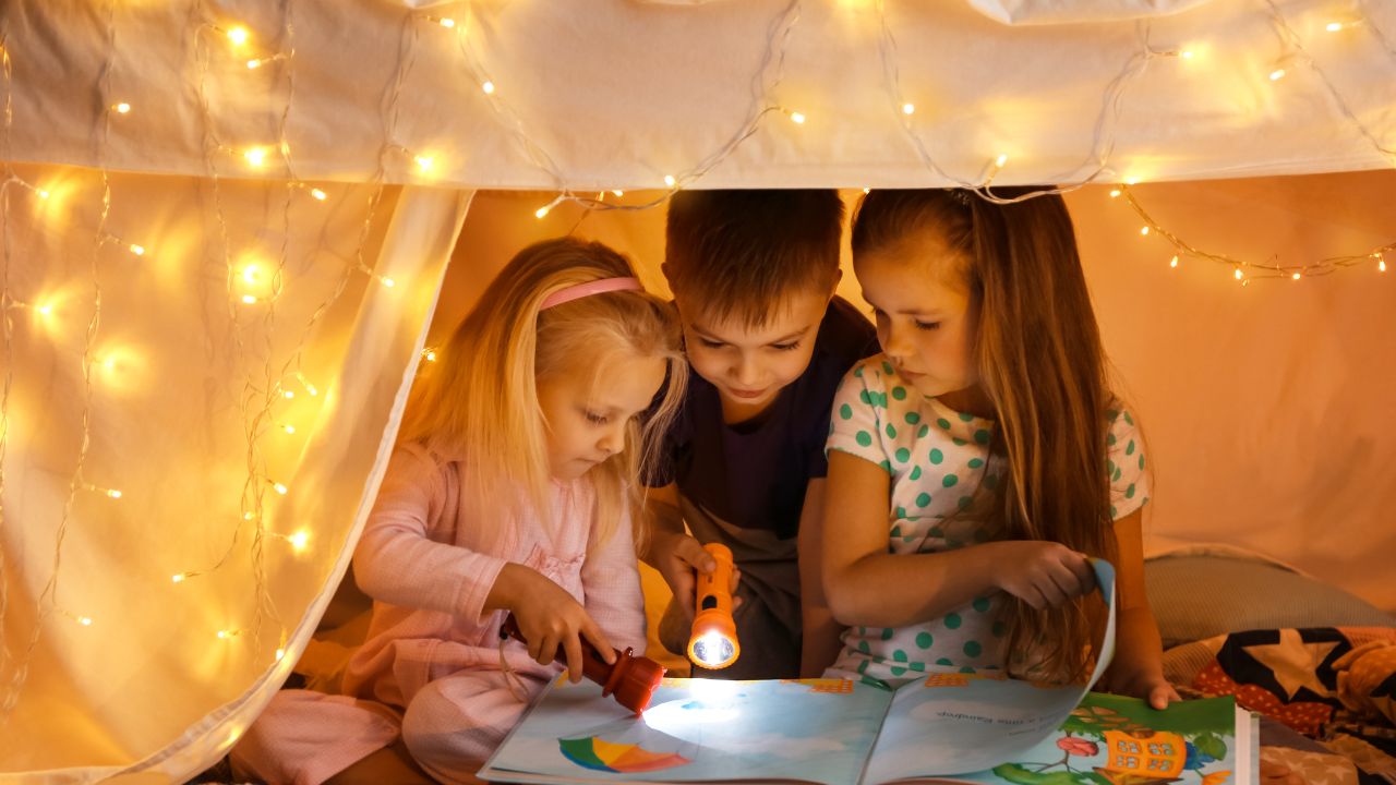 Image of three children in a lit up tent all reading a book with flashlights.