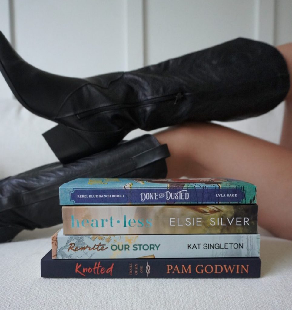 Halle wearing black cowboy boots that are behind a stack of books on a couch
