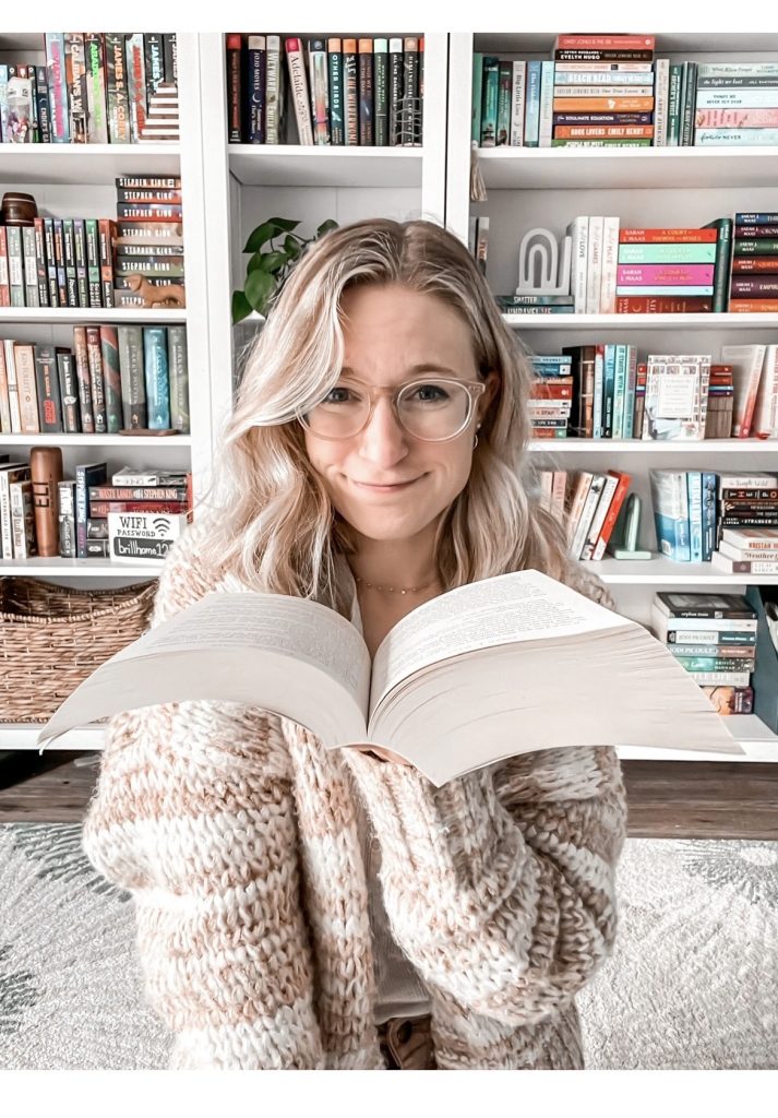 Jaclyn holding an open book in front of her bookshelves