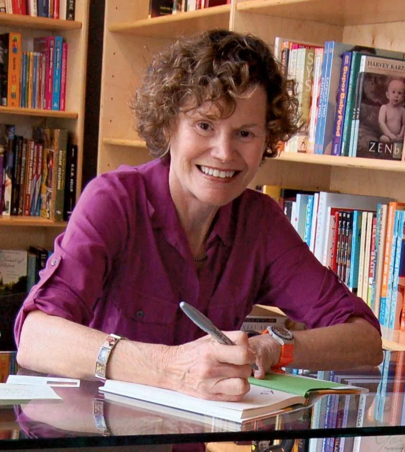 Judy Blume wearing a purple shirt and holding a pen in her hand.