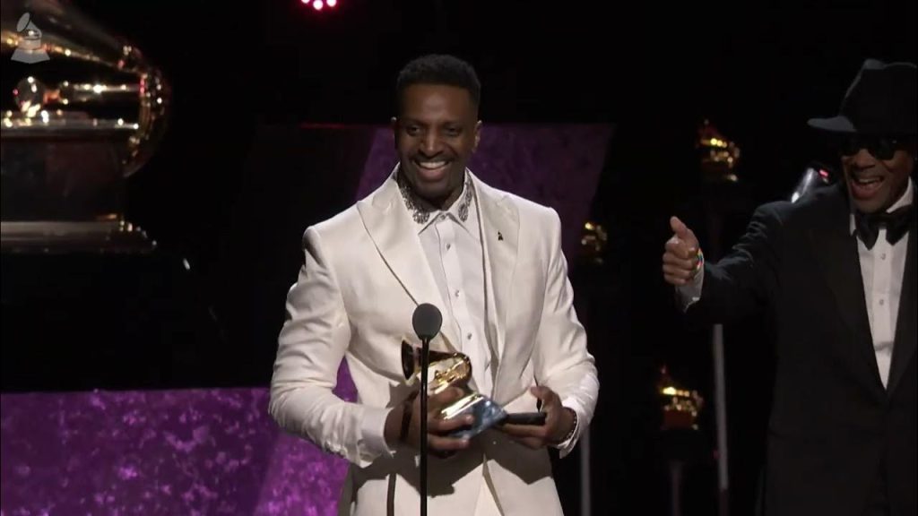 J. Ivy on the Grammy stage accepting an award in a white satin suit