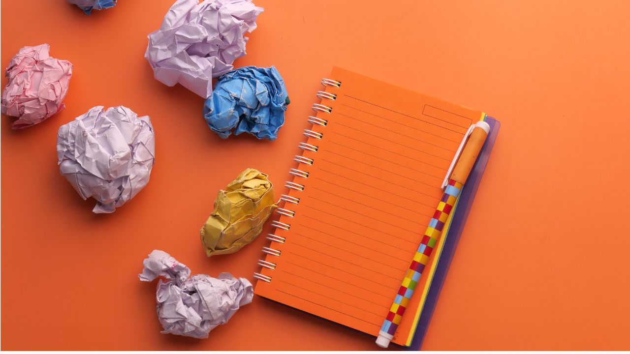 An orange notebook and several balled-up pieces of paper next to it.