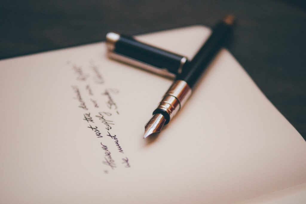 An uncapped pen resting on an open notebook with cursive on it.