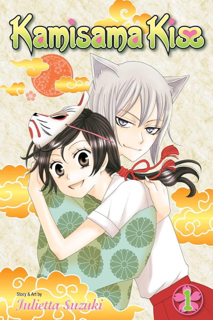 Kamisama Kiss by Julietta Suzuki manga book cover, showing a girl with a Japanese fox mask hugging a young man with fox ears on a background with orange clouds.