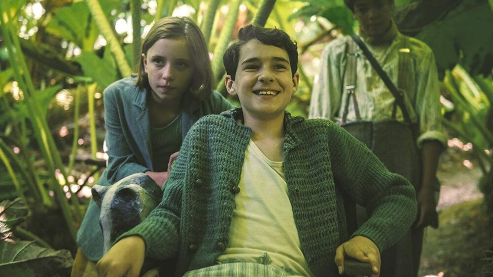 Mary and Dickon standing behind Colin sitting in his chair outside