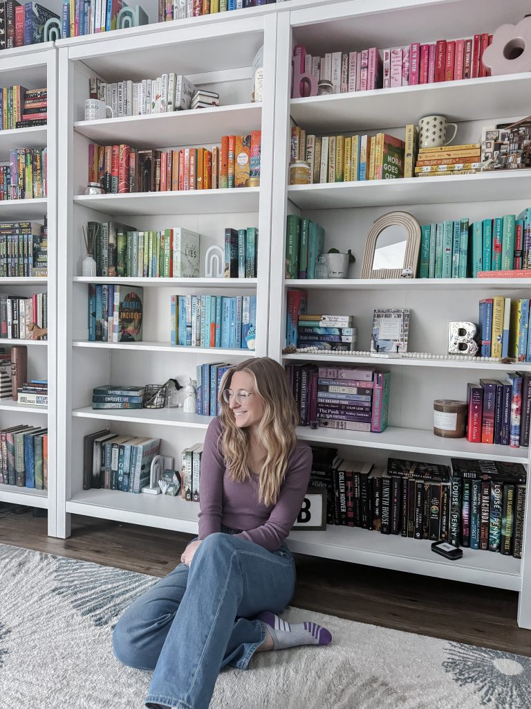Jaclyn sitting on the floor leaning against her bookshelves