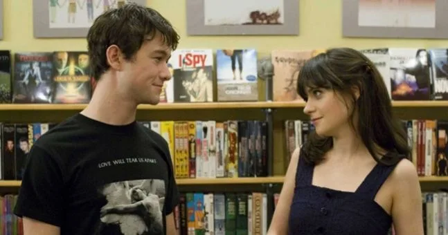 Man and woman dressed in black smiling at each other in front of a bookshelf