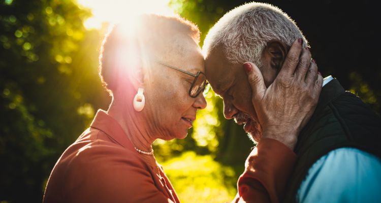 A person comforting another by placing their heads together with the sun in the background.
