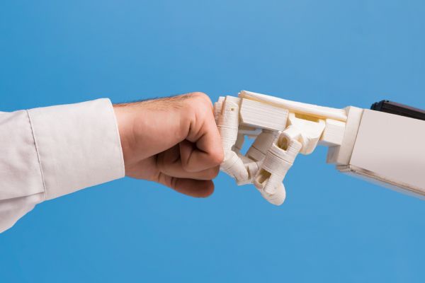 Human hand and robot hand coming together in a fist bump to symbolize connection and union.