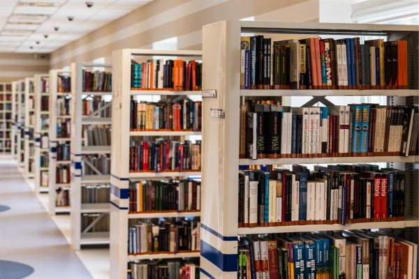 Rows of white library shelves stacked with many different types of books.