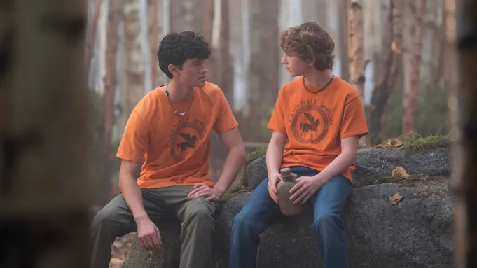 Two boys in orange shirts sitting next to one another. 
