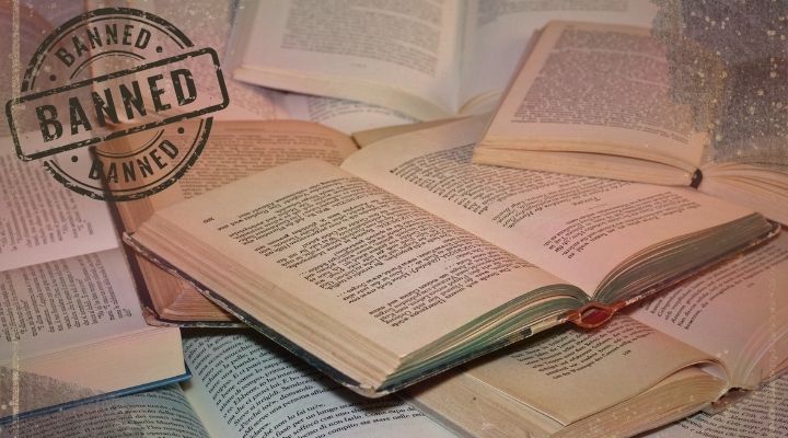 Numerous open books with a lot of words on the pages. The word banned in the top left corner and smudges of black in the bottom left and top right corner.