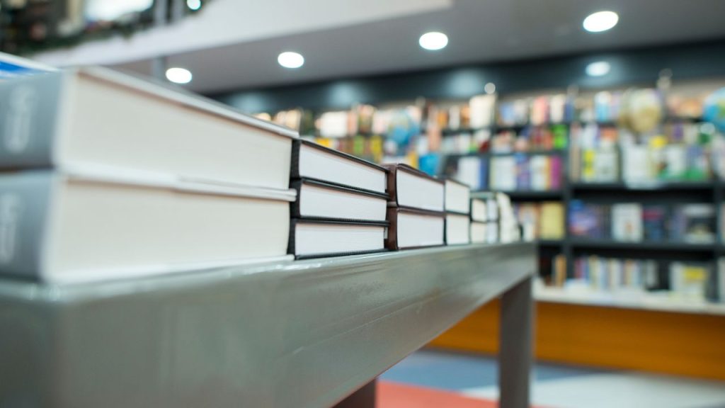 A gray, metal table at a bookstore is taken at the angle so that the bottom, plain white book ends are facing the image.
