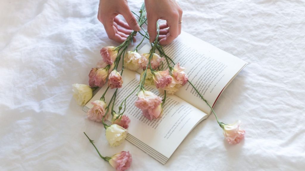 A book with hands placing flowers on top.
