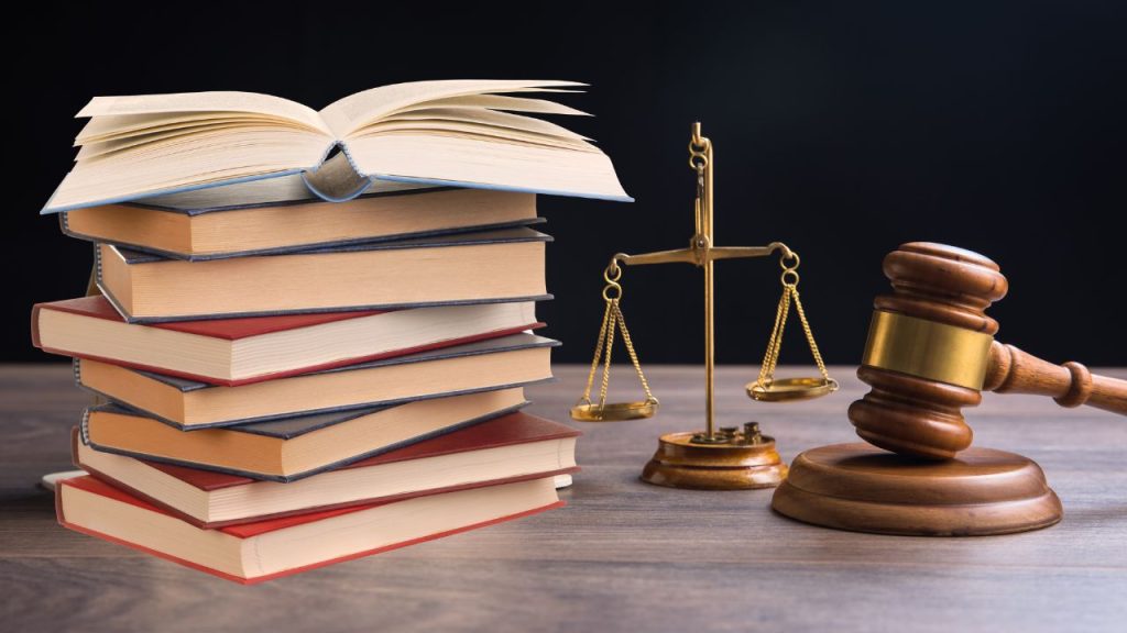 Stack of books next to a gavel with a balance scale between them.