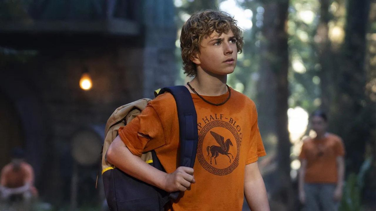 A boy in an orange t-shirt with a backpack on his shoulder.