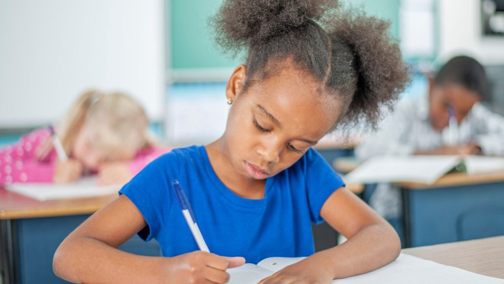 Little girl writing in a notebook in a classroom.