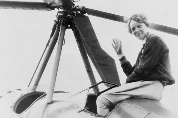 Earhart sitting in plane, waving to camera.