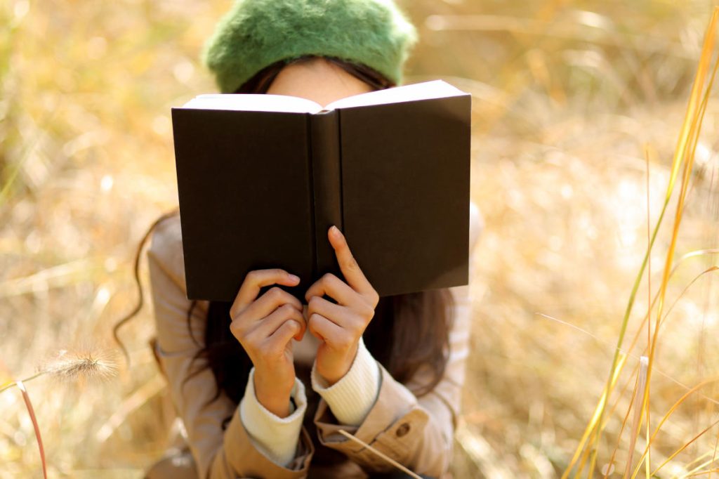 Woman reading in a field with the book open before her face.