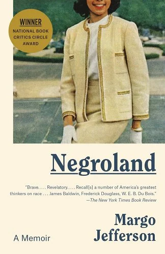 Image of a black woman in a 60s inspired female suit with white gloves and an empty parking lot in the background.
