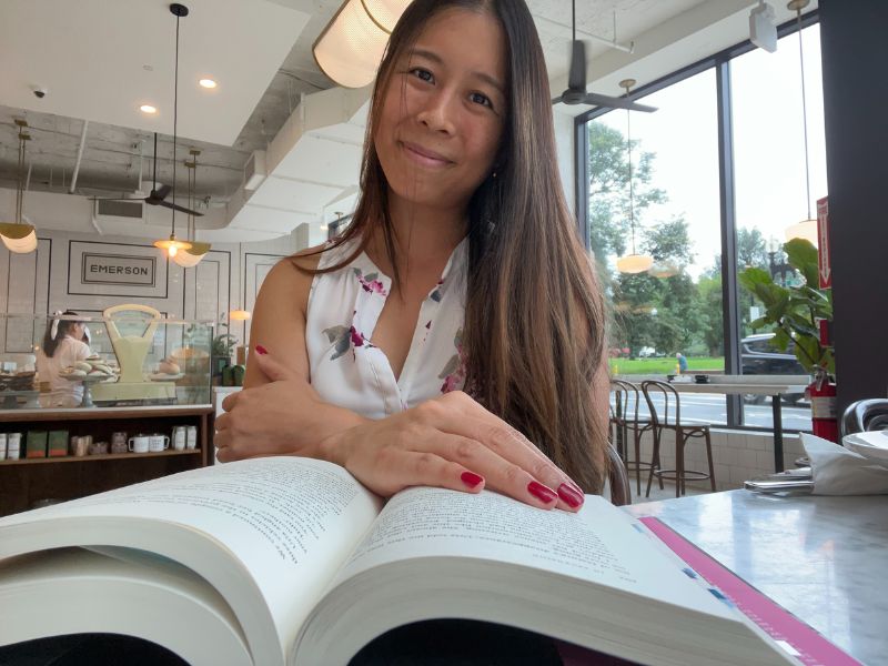 Boostagrammer Kristin Lee sits in a brightly lit cafe with her hand over a book.