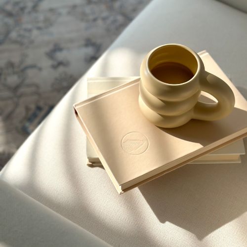a beige book stack with a beige mug with tea inside of it on a cream sofa