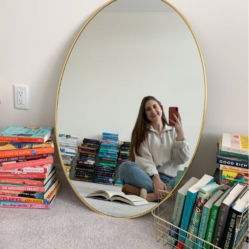 picture of Melissa taking a mirror selfie with her books all around her in piles and a book open in front of her.