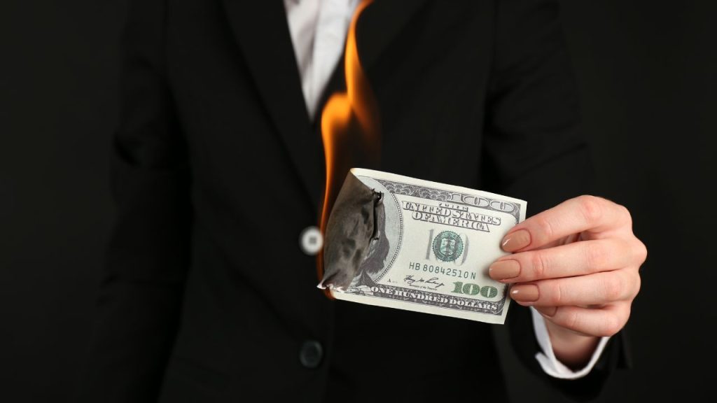 Person in suit holding a burning 100 dollar bill.