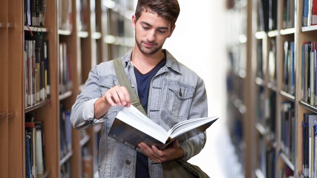 Man in a library reading a book.