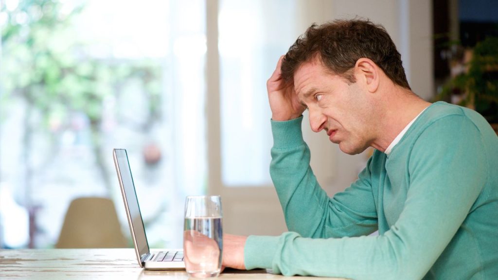 Man reading laptop looking confused.
