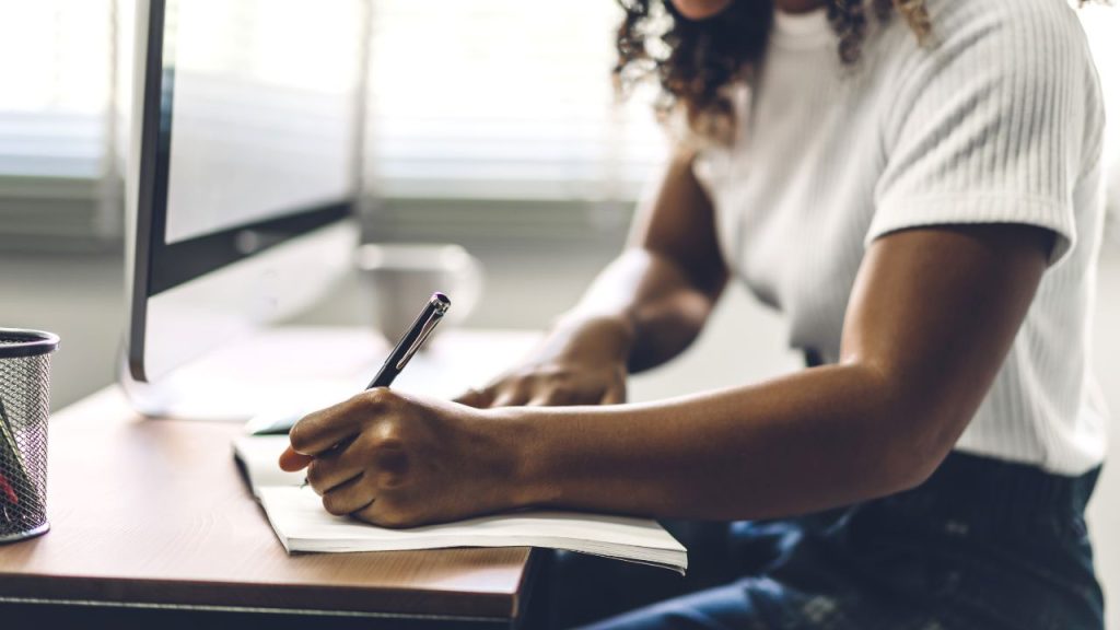 A woman writing on a notepad sitting at a desk.