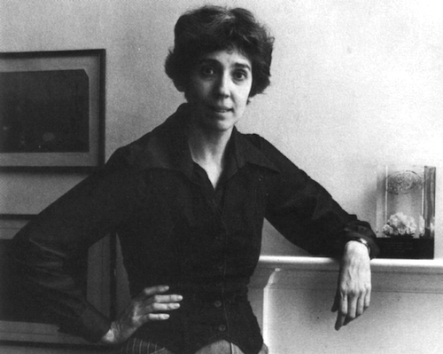 black and white photo of Joanna Russ leaning on a shelf with paintings in the background