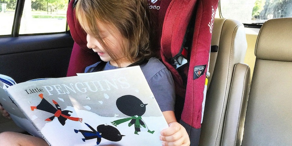A little girl sitting in a car reading 'Little Penguins.'