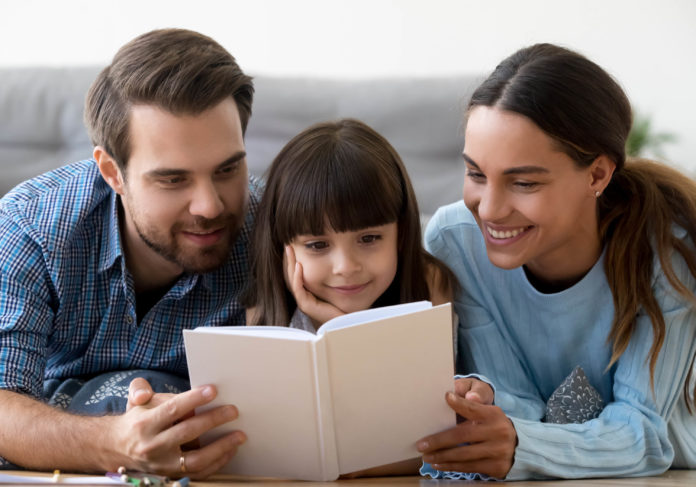 A woman, little girl, and man reading a book together.