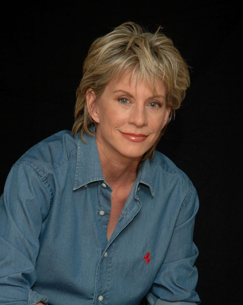 Patricia Cornwell wearing a button-up denim shirt, smiling, and looking ahead.