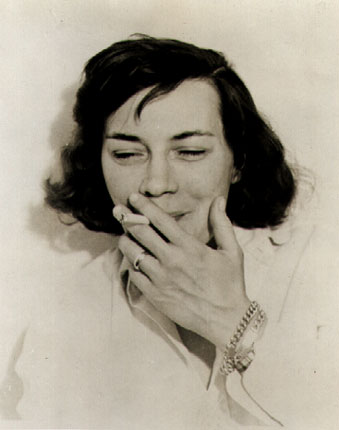 Patricia Highsmith grinning while she smokes a cigarette.