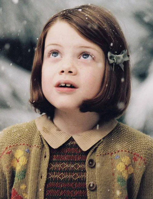 lucy looking up at the sky snowing in Narnia with a short brown bob and a green bow in her hair
