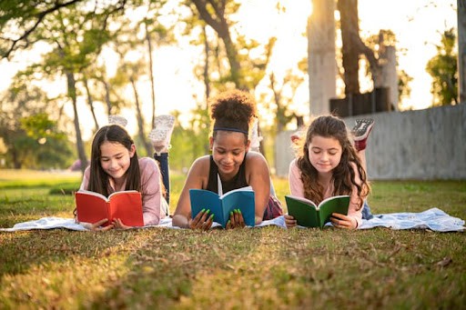 Three girls laying on a blanket and reading.