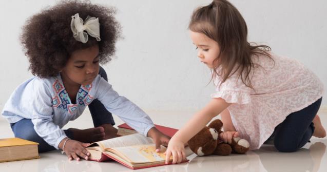 Two little girls sharing and reading a book.