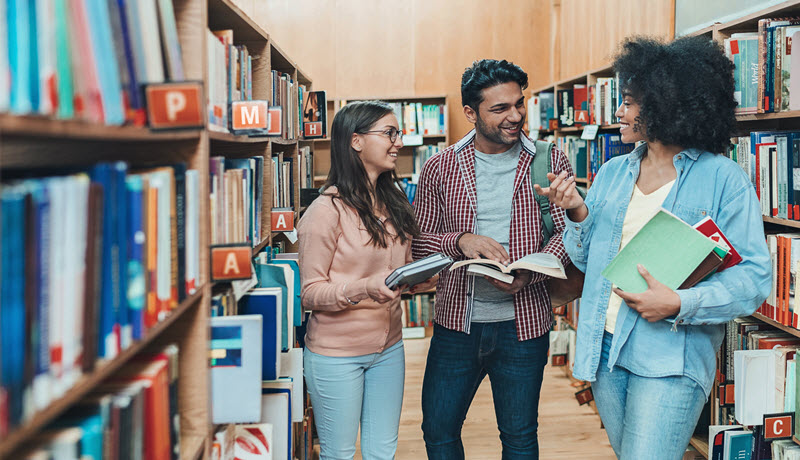 Three people standing and talking in a library.