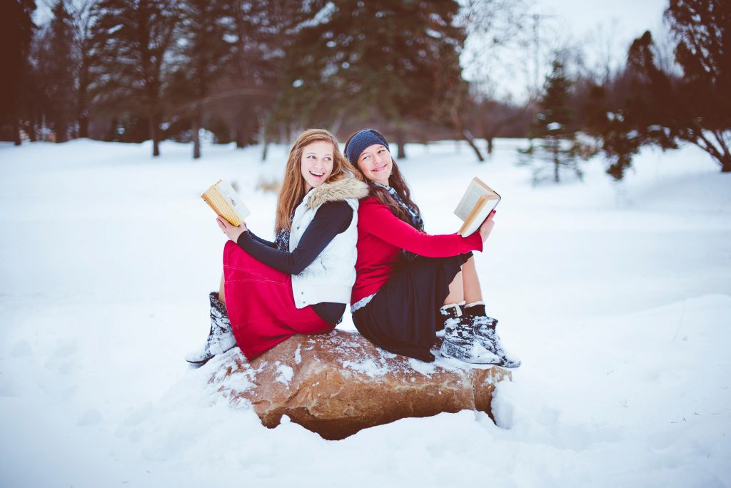 Two friends sitting and smiling while holding books.