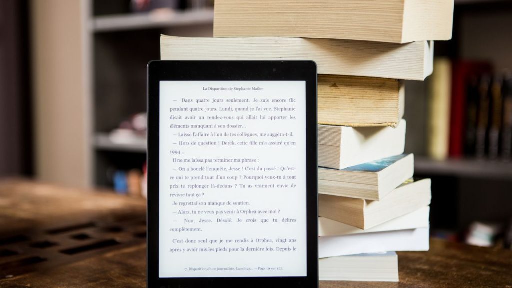 an ebook reader and hefty paperback books stacked up behind it.