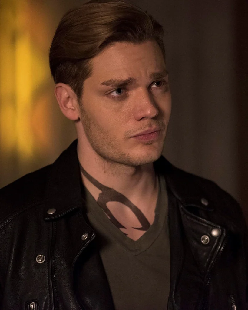 Jace Herondale with blonde hair and a black leather jacket looking off camera.