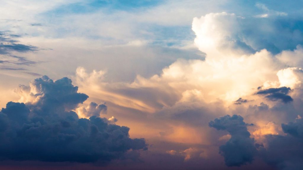 A morning sky with contrasting clouds at different heights. The morning sun peaks through the clouds, lighting them up orange in the middle, and shades of blue on the outside.