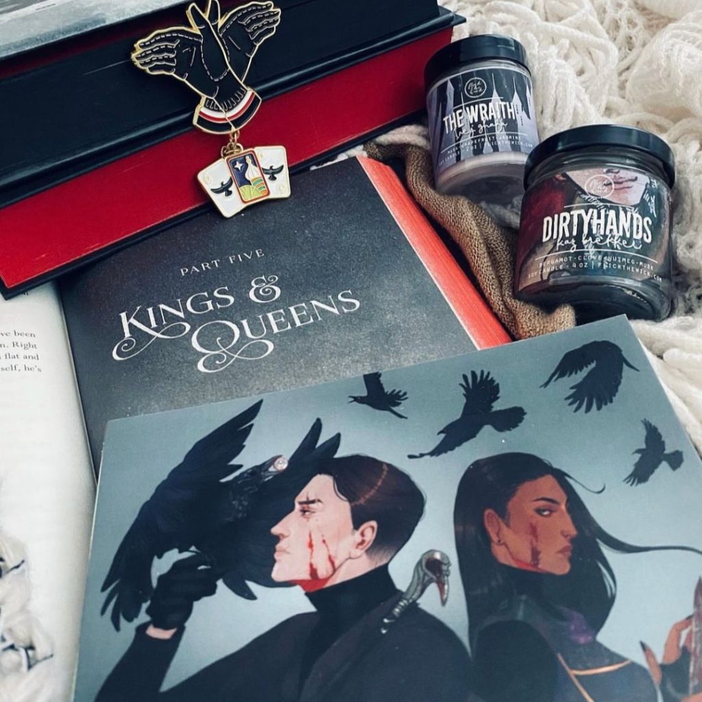 Merch from the Grishaverse from candles, brooches, books with red sprayed pages, and fan art are on display.