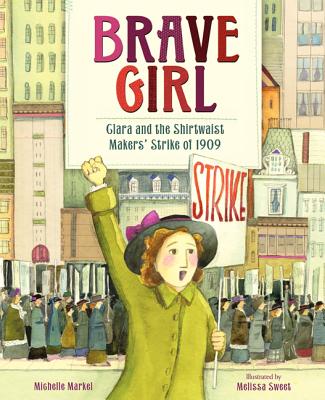 A woman in a green coat and a black hat with a pink bow holds a white sign that reads "Strike" in red paint against a background of city buildings with other women holding similar signs.