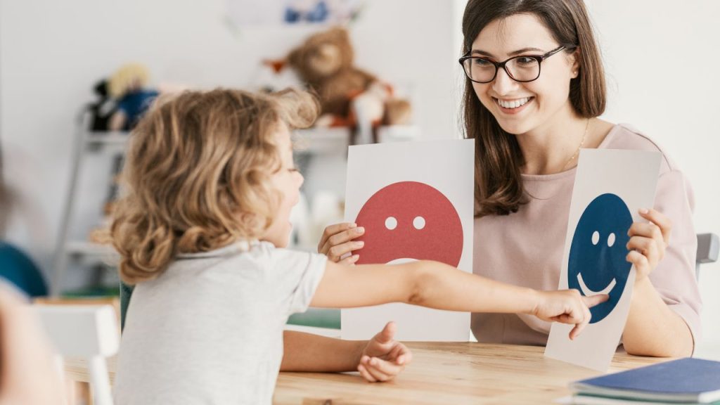 A little girl choosing a smiley face over sad face while laughing.