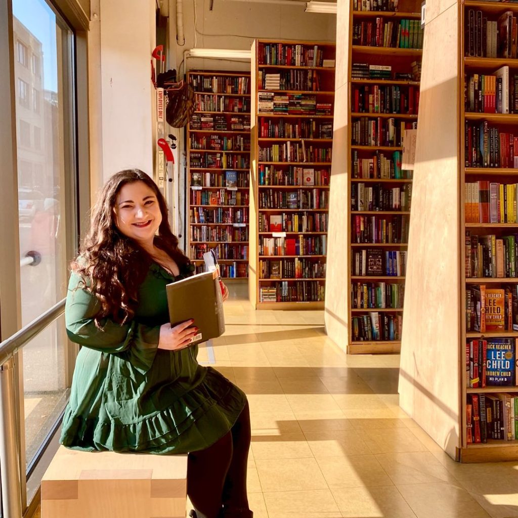 Bookstagrammer Ceci holding a book, alongside bookshelves filled with books.