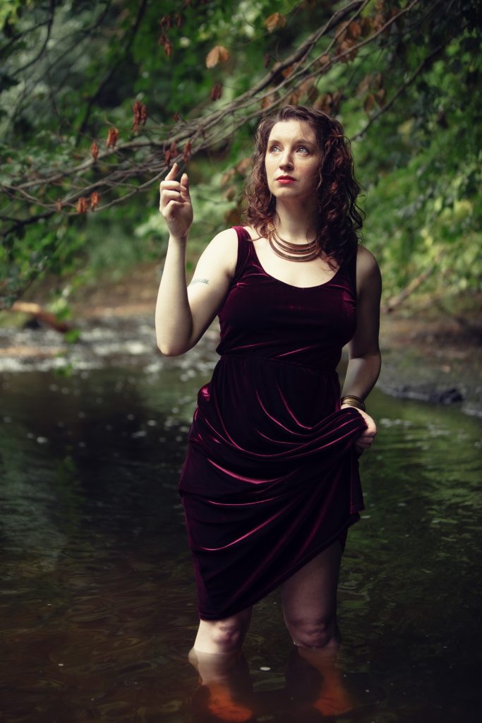 Emmie Mears reaching up a tree while hiking up their dress,