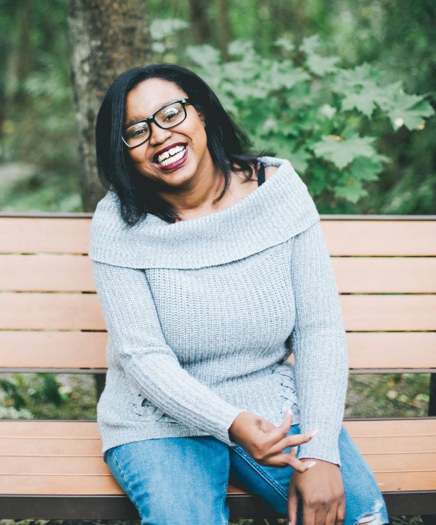 Keah Brown smiling while sitting on a bench outdoors.